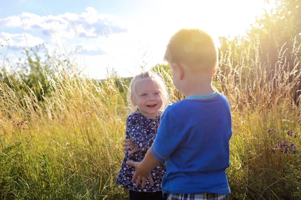 Bambini che si divertono e si abbracciano nell'erba verde con fiori, dorati — Foto Stock