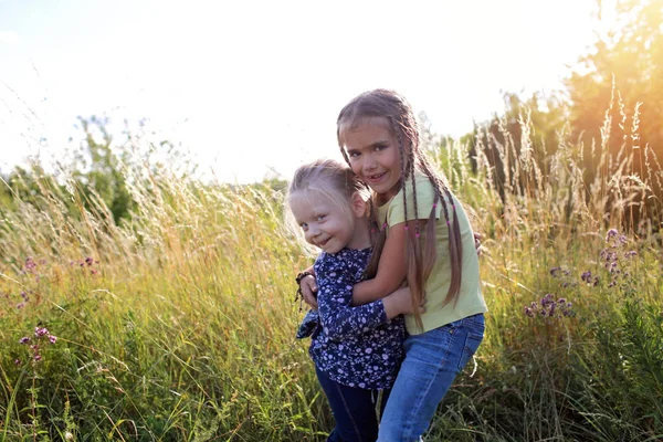 Bambini che si divertono e si abbracciano nell'erba verde con fiori, dorati — Foto Stock