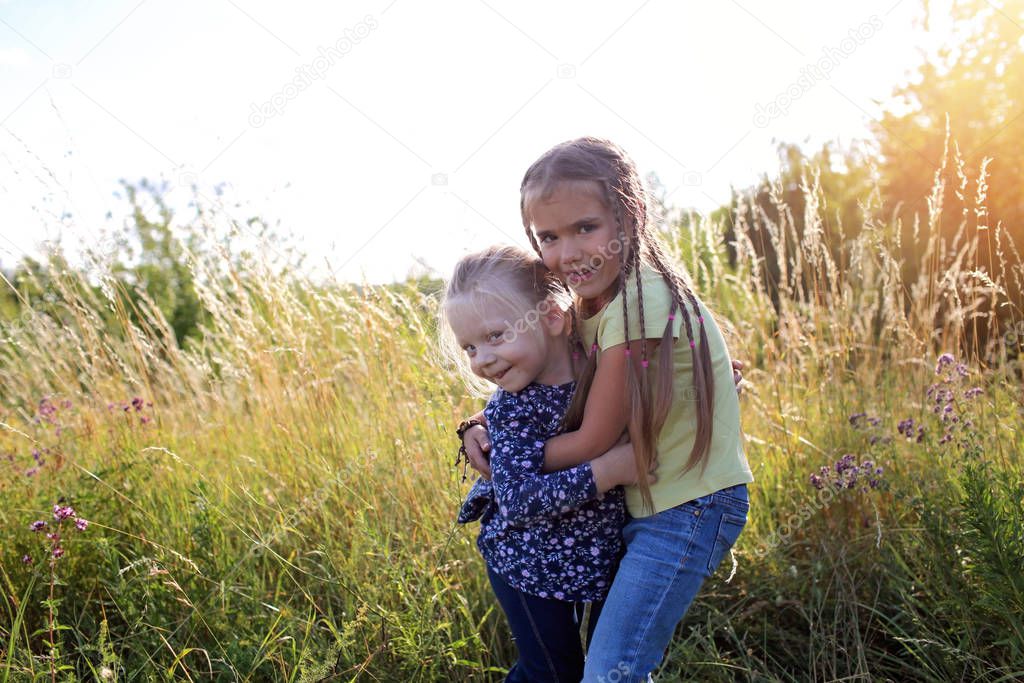 Kids having fun and hugs in the green grass with flowers, golden