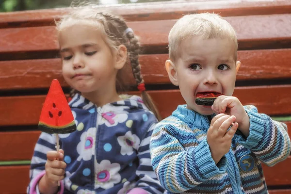 Dos niños comiendo caramelos de color rojo brillante con sabor a sandía en el —  Fotos de Stock