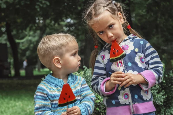 Dos niños comiendo caramelos de color rojo brillante con sabor a sandía en el — Foto de Stock