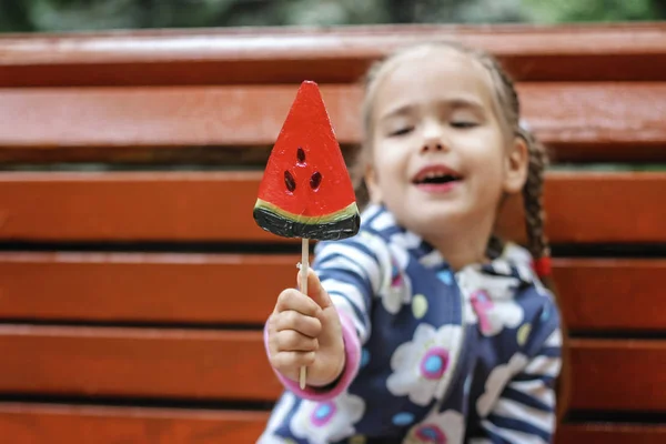 6-7 anos menina comendo doces vermelhos brilhantes com sabor de melancia i — Fotografia de Stock