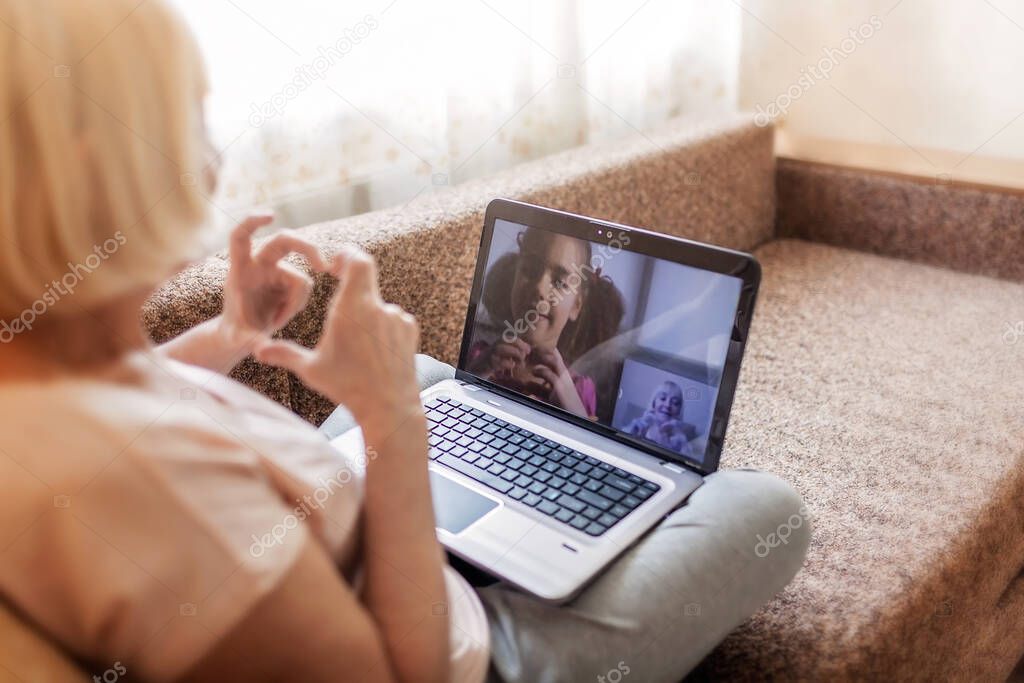 Cute girl talking with her grandmother within video chat on laptop, digital conversation, life in quarantine time, self-isolation