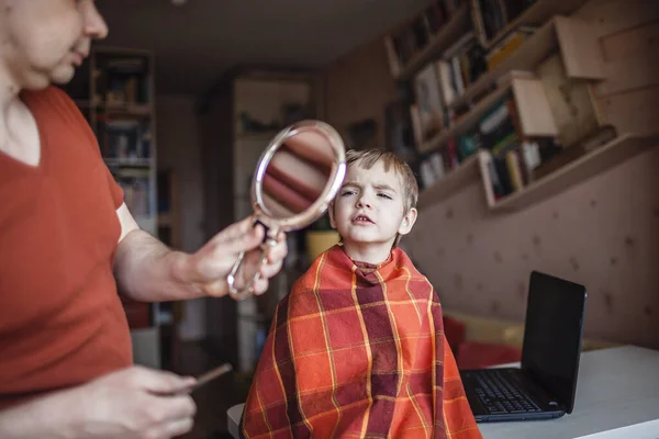中年父亲在家里自己剪头发给他的小儿子看 在笔记本电脑上播放视频 上网上发型课 在关禁闭期间待在家里和生活 — 图库照片