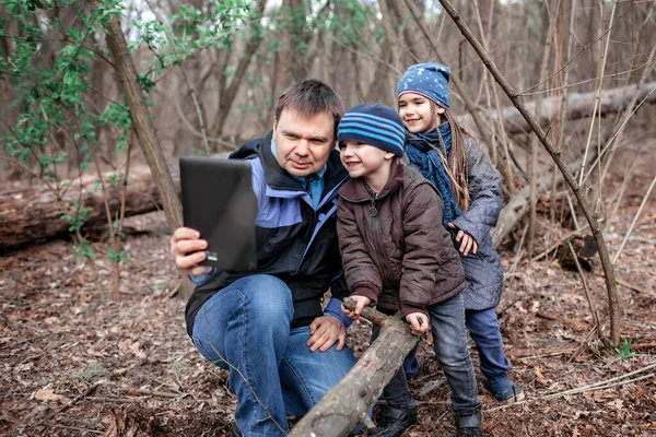Middle aged father with children walking in the wild forest and connecting with the grandmother to show video report via online chat, online conversation during lockdown time, outdoor lifestyle