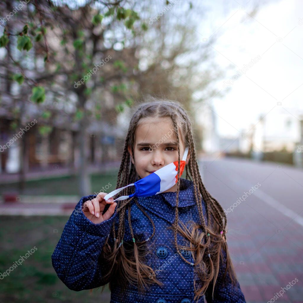 Happy little girl wearing off the respirator medical mask in national France colors because of the end of quarantine in the country, happiness and hope, stop virus spreading, outdoor lifestyle