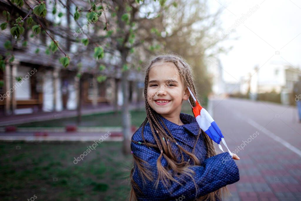 Happy little girl wearing off the respirator medical mask in national France colors because of the end of quarantine in the country, happiness and hope, stop virus spreading, outdoor lifestyle