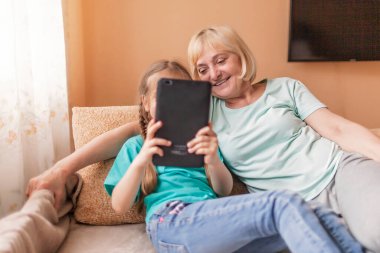 Mutlu torun, büyükannesine portatif tablet kullanmayı öğretiyor ve selfie çekiyor, online hayat, koronavirüs salgınından sonra yeni normal, mutlu gümüş sörfçü dijital yerli nesil.