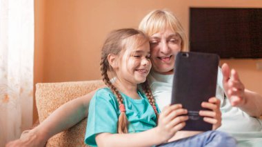 Mutlu torun, büyükannesine portatif tablet kullanmayı öğretiyor ve selfie çekiyor, online hayat, koronavirüs salgınından sonra yeni normal, mutlu gümüş sörfçü dijital yerli nesil.