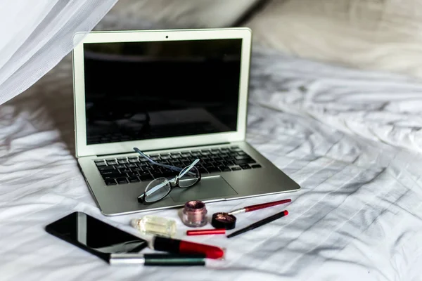 Espacio de trabajo nómada digital en la cama blanca con portátil, teléfono y gafas . Imágenes De Stock Sin Royalties Gratis