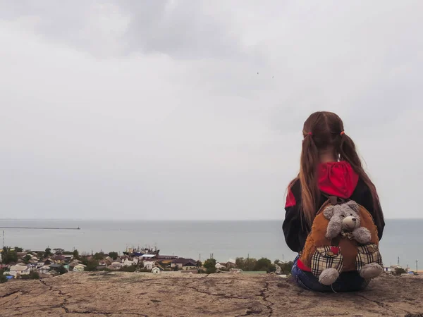 A beautiful girl is sitting and looking at the city and the sea. — Stock Photo, Image