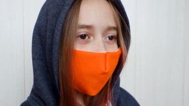 Yüzü maskeli bir genç öksürüyor. Coronavirus ve grip salgını konsepti. Kız, maske takıyor, göz kırpıyor ve etrafına bakıyor..