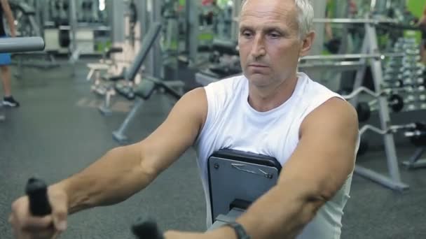Old man is engaged on simulators in gym — Stock Video