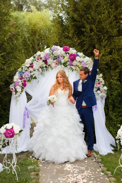 Recién casados de pie cerca del arco de la boda —  Fotos de Stock