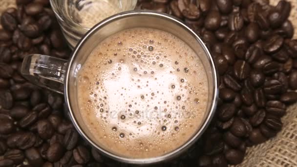 Coffee grains around the glass cup of cappuccino and a glass of water on sacking — Stock Video