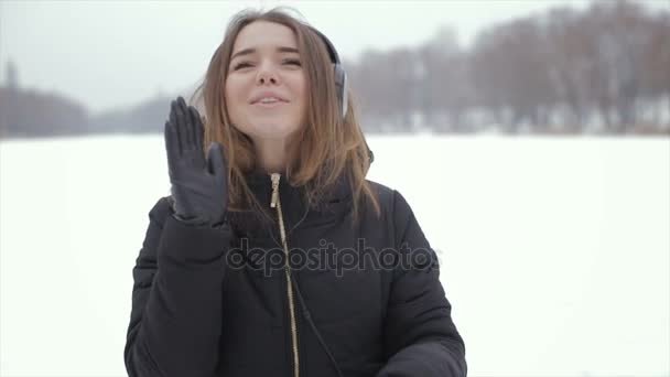 La fille joyeuse dans les écouteurs d'hiver écoutant de la musique, debout dans la neige — Video