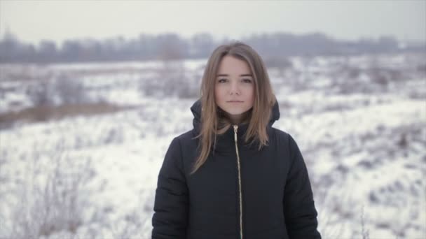 Het meisje in een zwarte jas op een achtergrond van een winter veld — Stockvideo