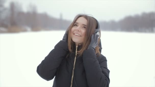 A menina alegre em fones de ouvido de inverno ouvindo música, de pé na neve — Vídeo de Stock