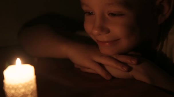 Un mignon garçon souriant regardant une bougie allumée — Video