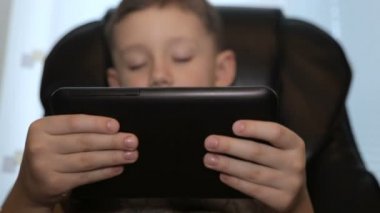 Bir deri sandalyede çocuk elinde bir tablet ile