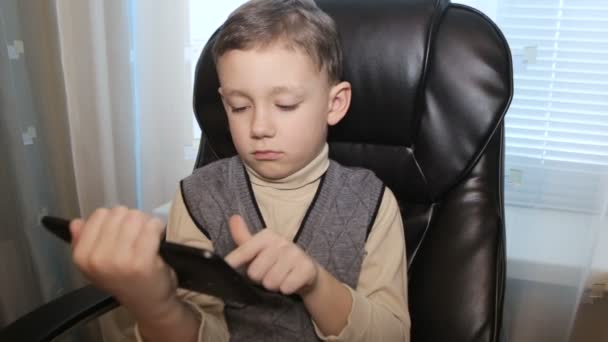 Хлопчик у шкіряному кріслі з таблеткою в руках — стокове відео
