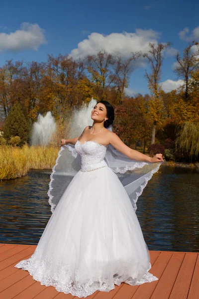 De bruid in een rijke trouwjurk staat op de pier — Stockfoto