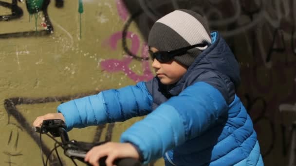 Хлопчик у сонцезахисних окулярах сидить на велосипеді. Повний HD відео — стокове відео