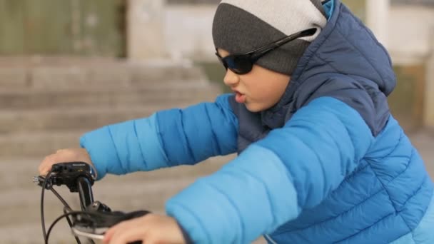 Bir çocuk güneş gözlüğü takıyor bir bisiklet üzerinde oturur. Dolu hd video — Stok video