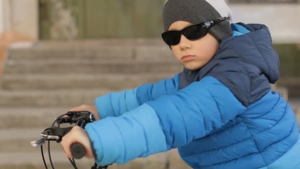 Bir çocuk güneş gözlüğü takıyor bir bisiklet üzerinde oturur. Dolu hd video — Stok video