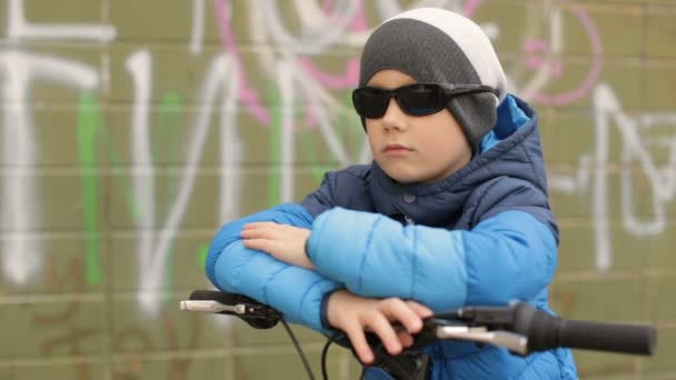 Un ragazzo con gli occhiali da sole si siede su una bicicletta.Video hd completo — Video Stock