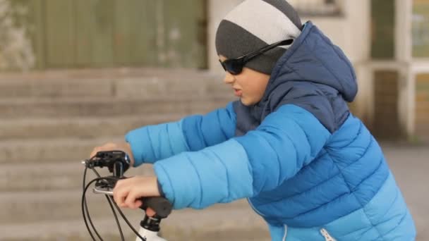 Хлопчик у сонцезахисних окулярах сидить на велосипеді. Повний HD відео — стокове відео