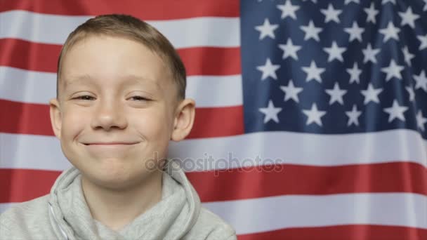 Das Porträt des Jungen vor dem Hintergrund des amerikanischen Banners. Nahaufnahme — Stockvideo