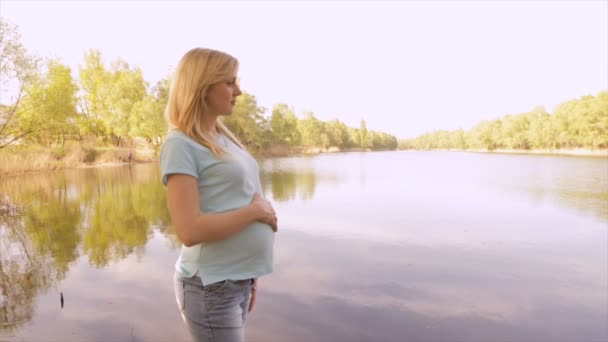 Chica embarazada en un día soleado cerca de un lago — Vídeo de stock