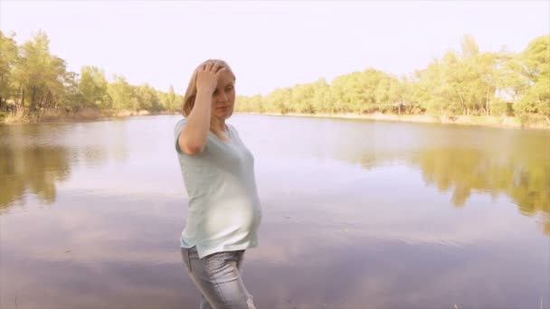 Fille enceinte par une journée ensoleillée près d'un lac — Video