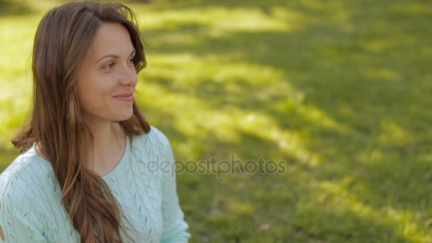 Cheerful girl in the park sits on the green grass — Stock Video