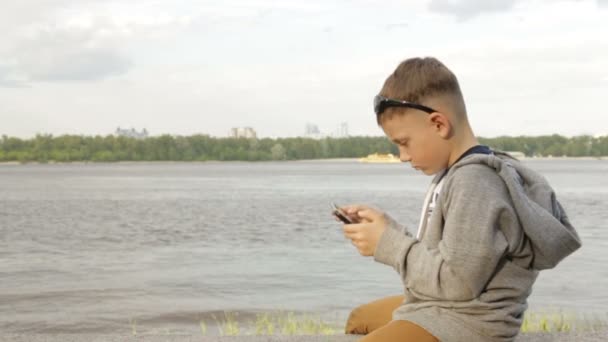 Un niño está jugando en una tableta cerca del mar — Vídeo de stock