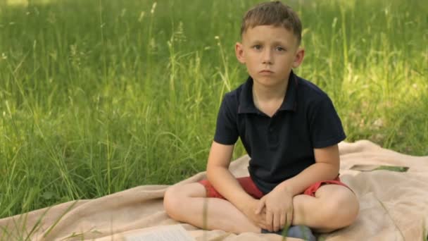 Niño triste sentado en el parque en un prado — Vídeo de stock