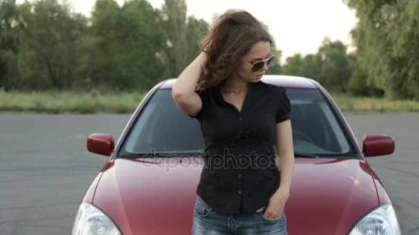 Девушка в солнечных очках позирует на фоне красной машины — стоковое видео