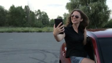 Bir kız kendini fotoğrafı bir tablet ile bir kırmızı araba arka plan üzerine alır.