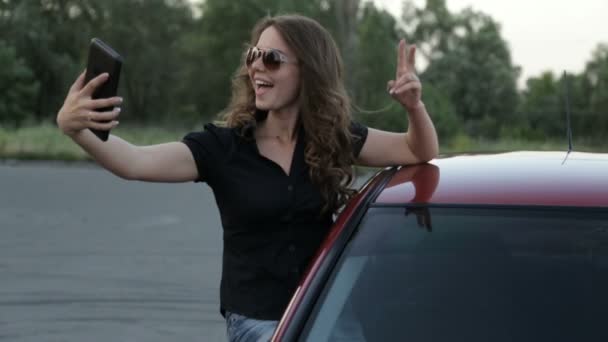여자는 빨간 자동차 배경 타블렛으로 자신의 사진을 걸립니다. — 비디오