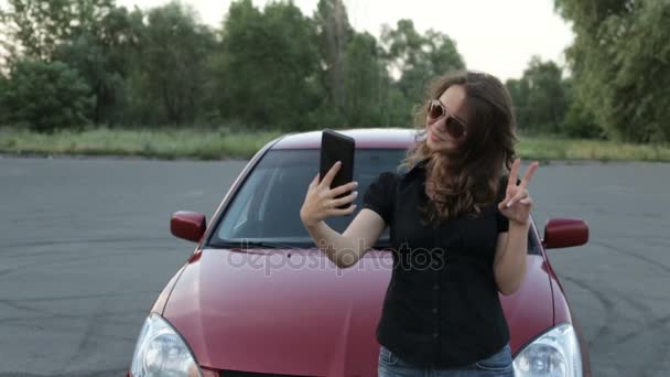 Uma menina tira uma foto de si mesma com um tablet em um fundo de carro vermelho — Vídeo de Stock