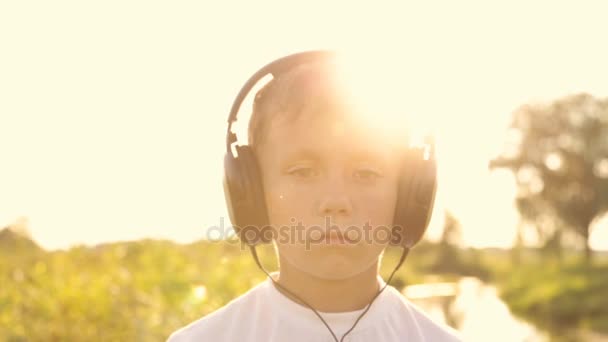 Jongen luisteren naar muziek via koptelefoons in de natuur onder de zonsondergang — Stockvideo