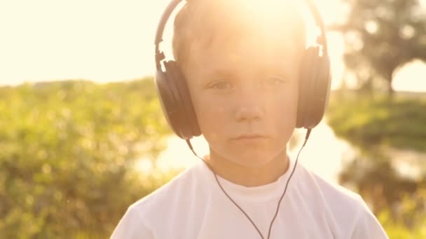 Menino ouvindo música através de fones de ouvido na natureza sob o pôr do sol — Vídeo de Stock