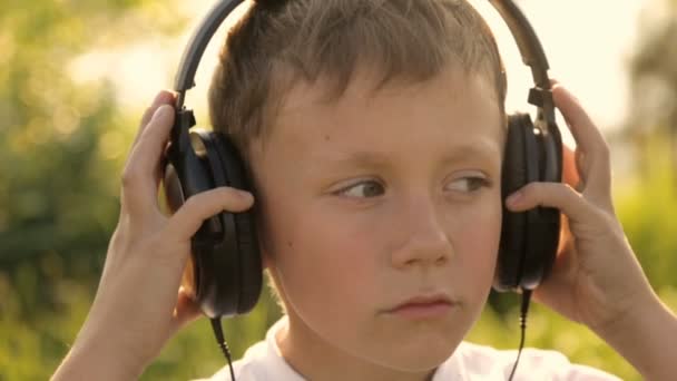 夕日の下で自然の中でヘッドホンで音楽を聞いている少年 — ストック動画