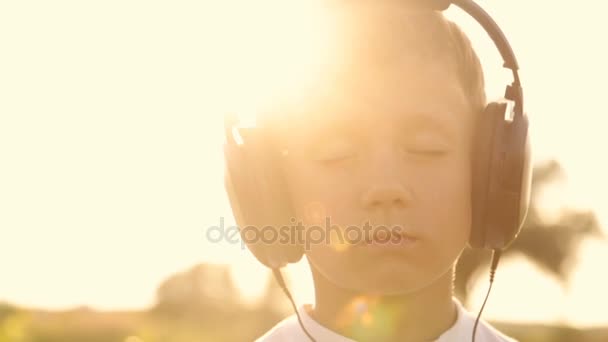 Jongen luisteren naar muziek via koptelefoons in de natuur onder de zonsondergang — Stockvideo