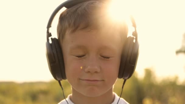 Menino ouvindo música através de fones de ouvido na natureza sob o pôr do sol — Vídeo de Stock
