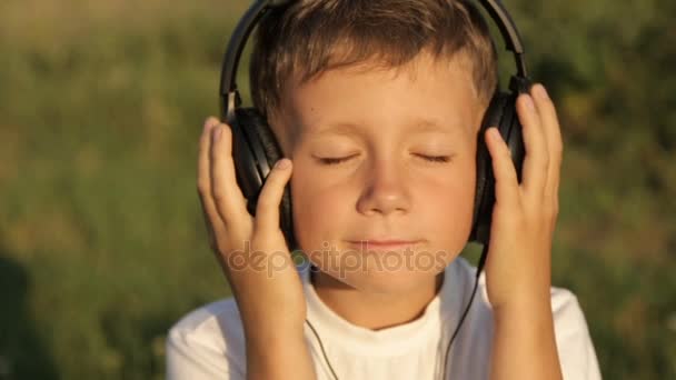 Niño escuchando música a través de auriculares en la naturaleza bajo el atardecer — Vídeos de Stock