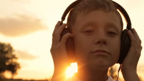 Niño escuchando música a través de auriculares en la naturaleza bajo el atardecer — Vídeos de Stock