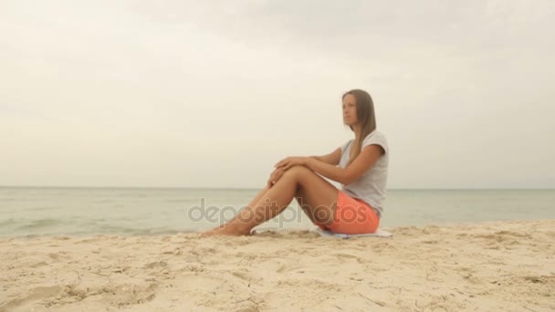 Una chica se sienta en la arena y mira al mar — Vídeos de Stock