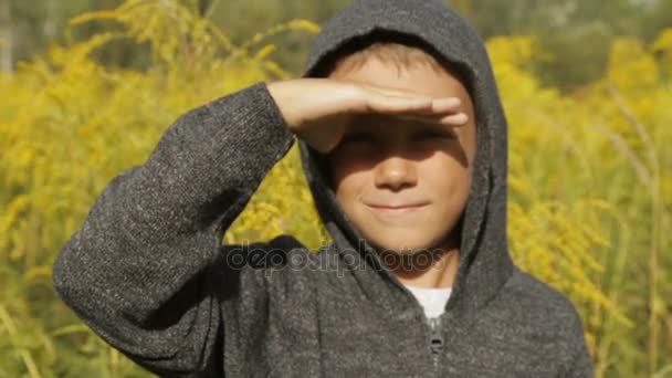 Um menino bonito em uma camisola cinza com um capuz ao ar livre — Vídeo de Stock